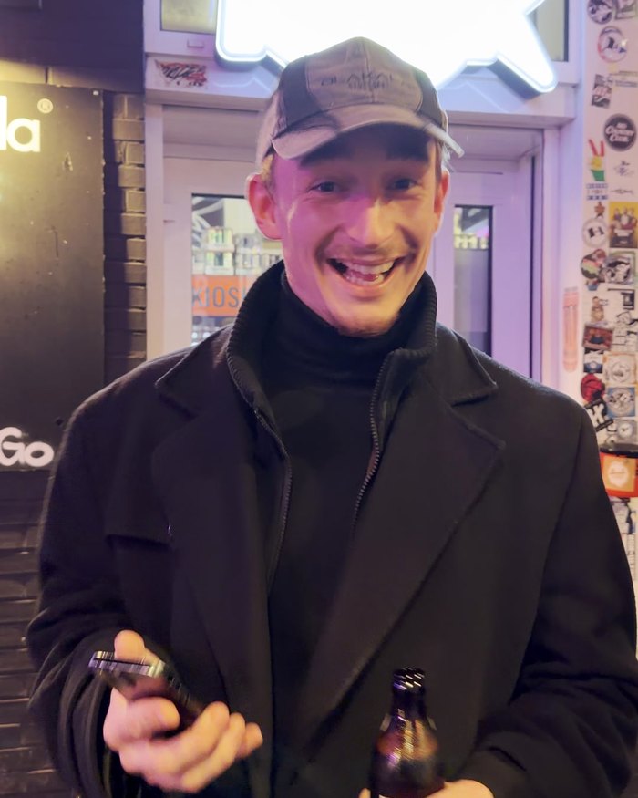 Ein Teilnehmer mit Mütze und Bier grinst vor einer Späti-Tür