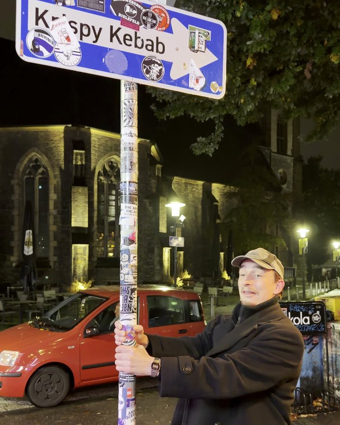 Ein Teilnehmer hält sich nachts an einem Straßenschild fest, im Hintergrund eine beleuchtete Kirche