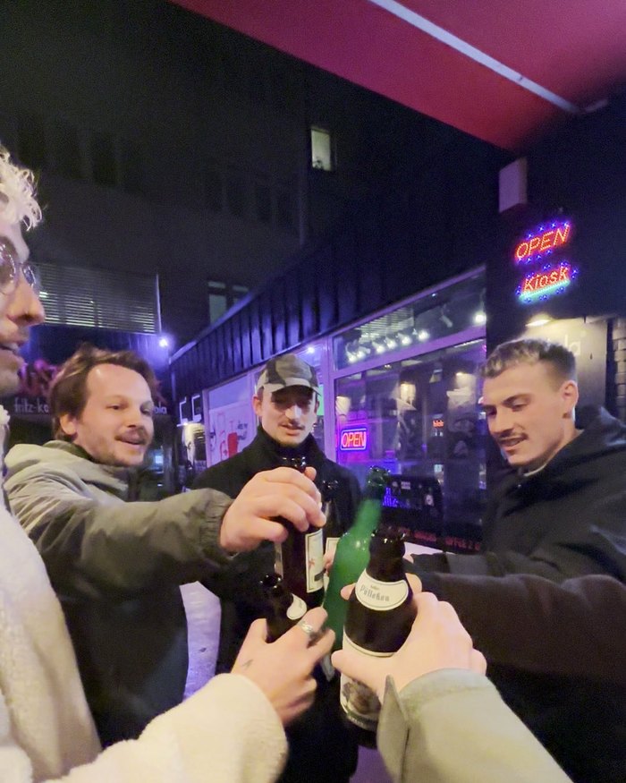 Eine Gruppe stößt nachts vor einem Späti mit Bierflaschen an